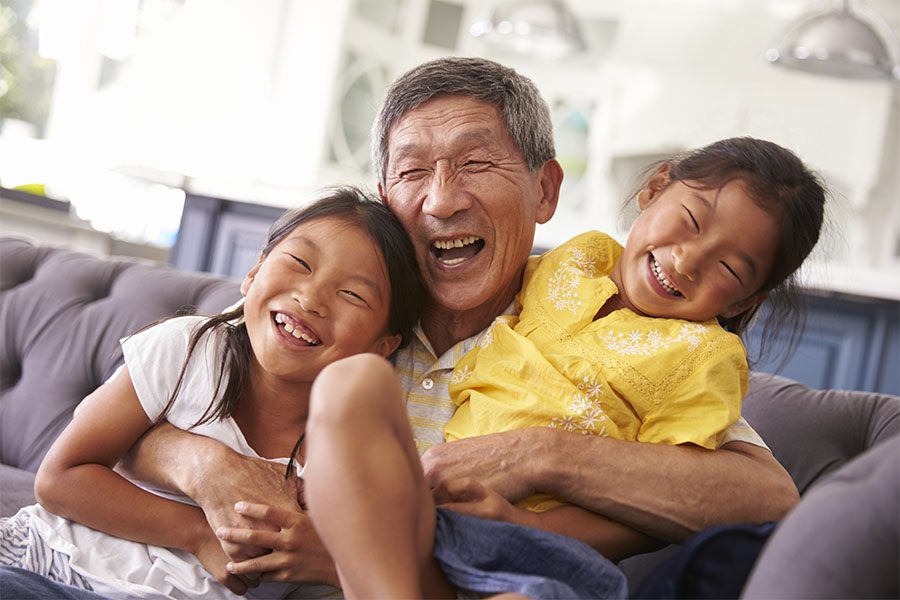 Contact - Portrait of a Cheerful Grandfather Hugging His Two Smiling Granddaughters While Sitting in the Living Room