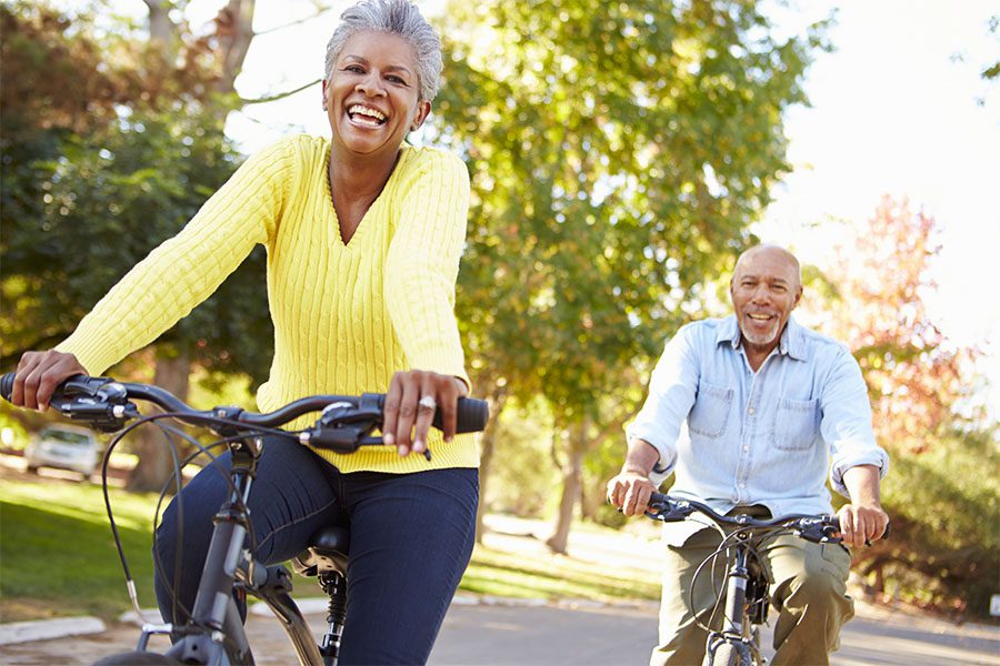 Health and Medicare - Cheerful Senior Couple Having Fun Riding Their Bikes Through a Quiet Neighborhood on a Sunny Day