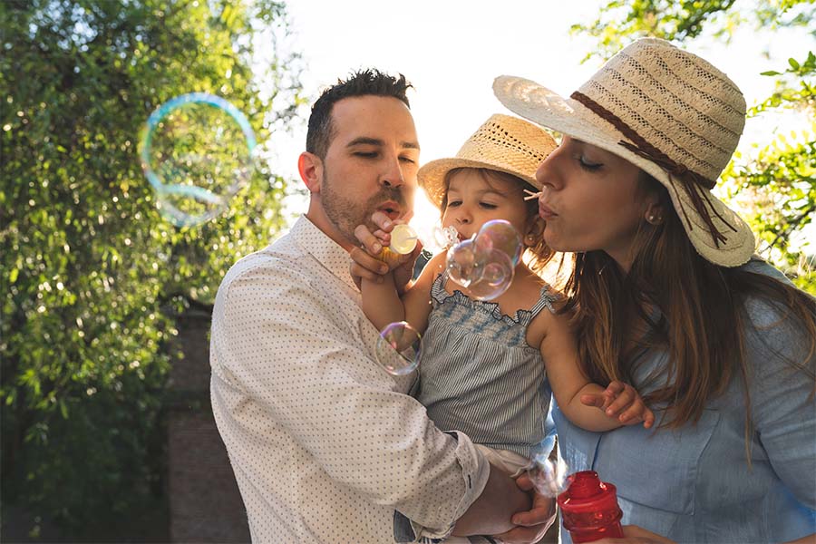 Individual Life Insurance - Portrait of Parents Holding Their Daughter While Blowing Bubbles Outside in the Backyard on a Sunny Summer Day