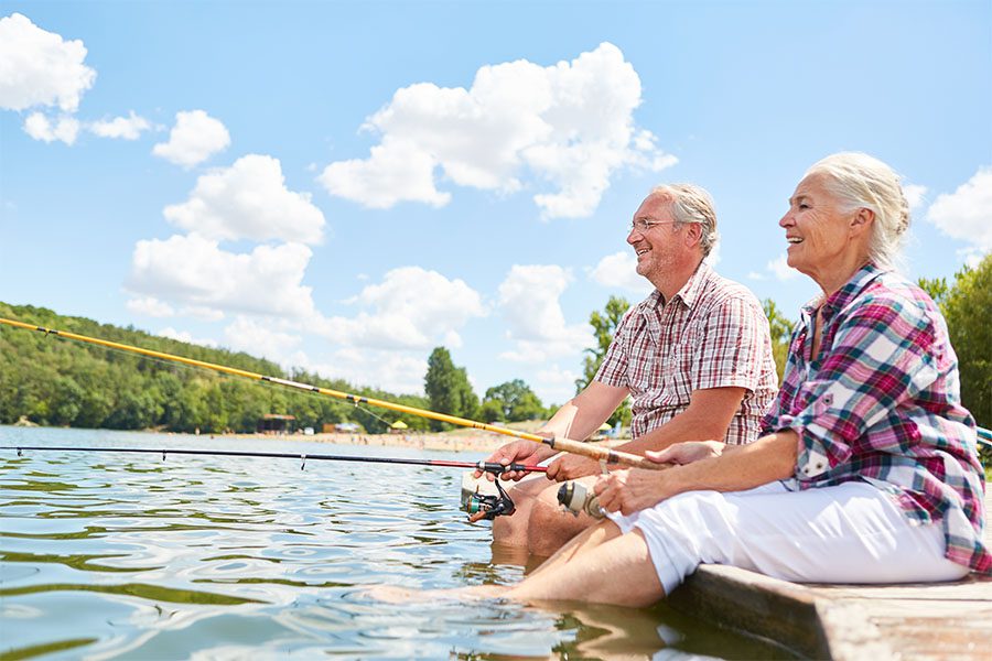 Refer a Friend - Portrait of a Cheerful Senior Couple Fishing Together While Sitting on a Dock with Their Feet in the Water