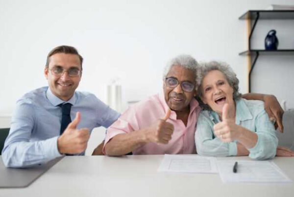 Blog - Older couple Sitting Next to a Professional and They Are all Giving a Thumbs Up to the Camera While Sitting at a White Desk
